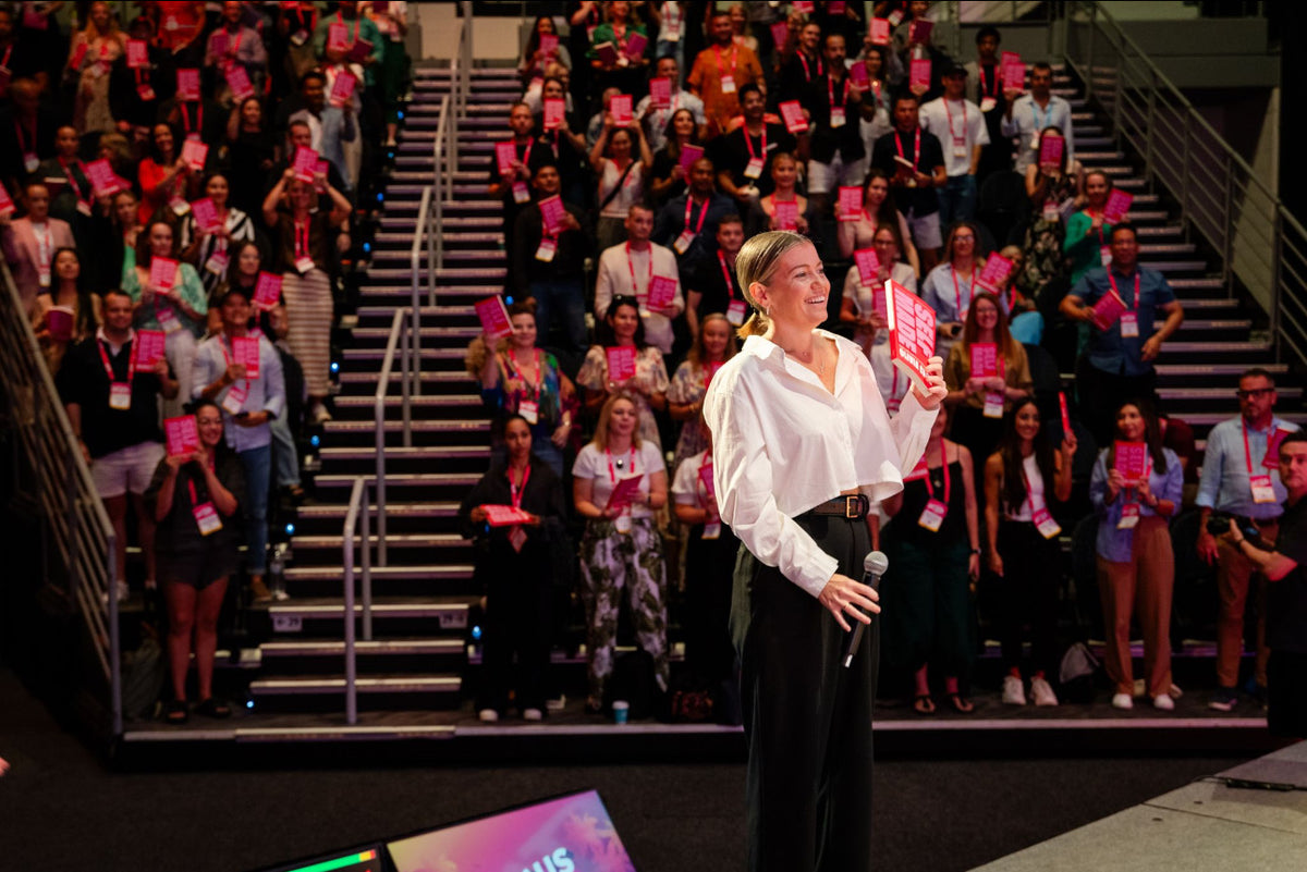 Olivia Carr on stage holding Self-Made in front of a full auditorium.