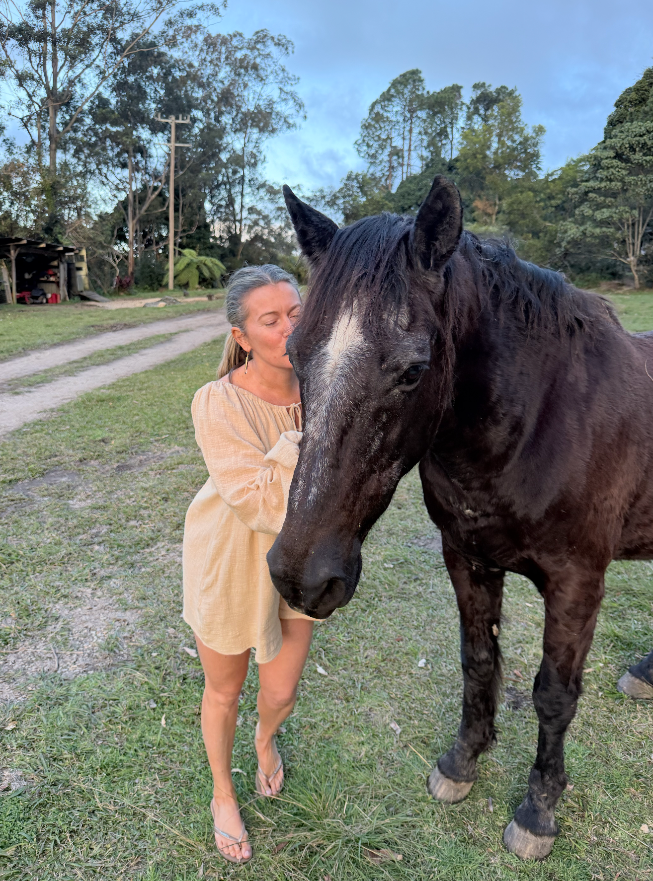 Olivia Carr leaning in close to a horse, eyes closed, outdoors at dusk.