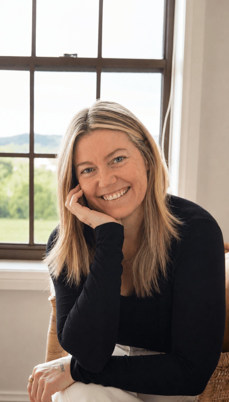 Olivia Carr seated by a window, smiling, chin resting on her hand.