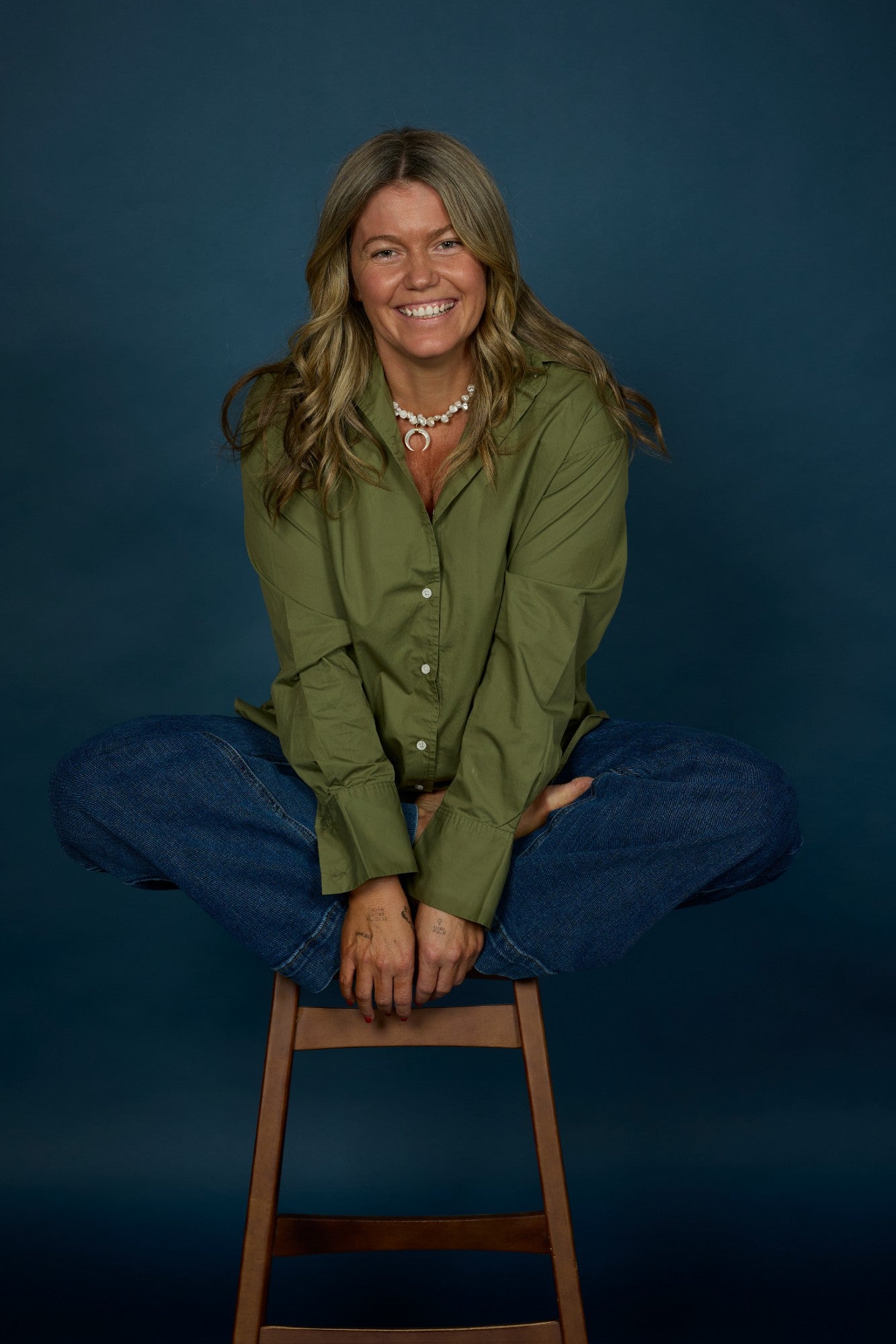 Olivia Carr, smiling, sitting cross-legged against a dark teal background.